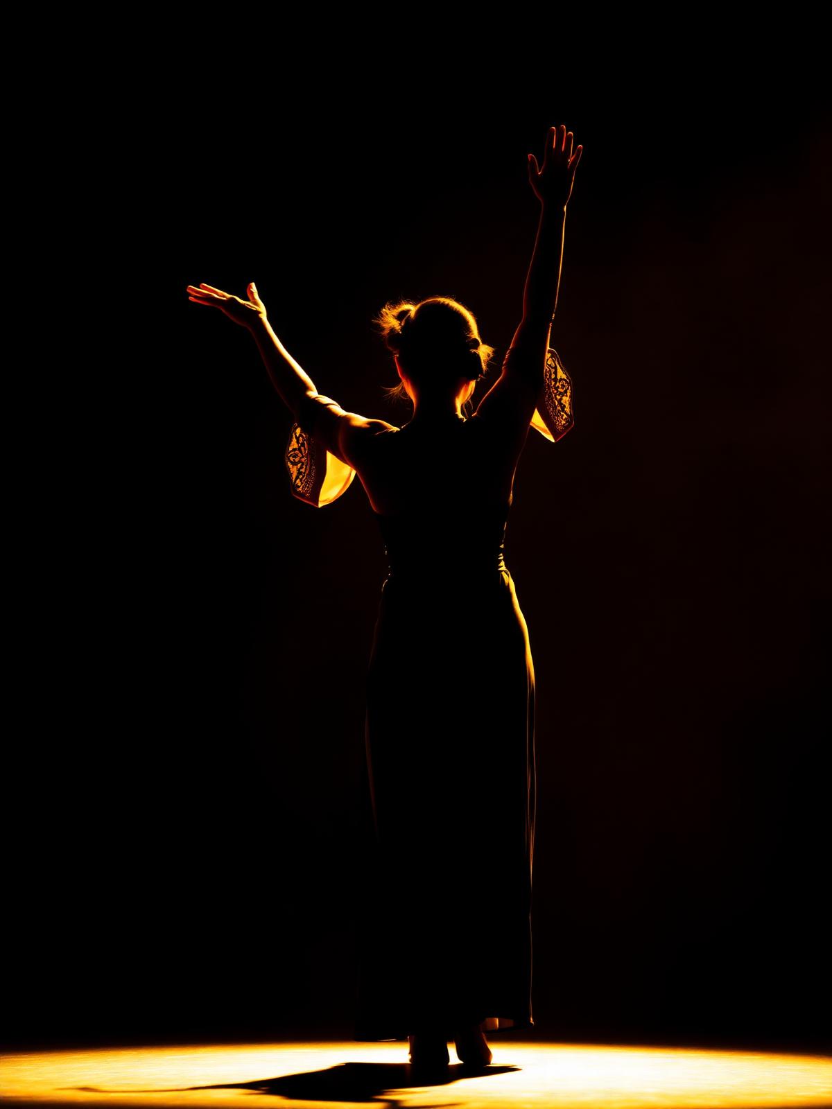 Silhouette of a Mayyas dancer beneath a warm spotlight